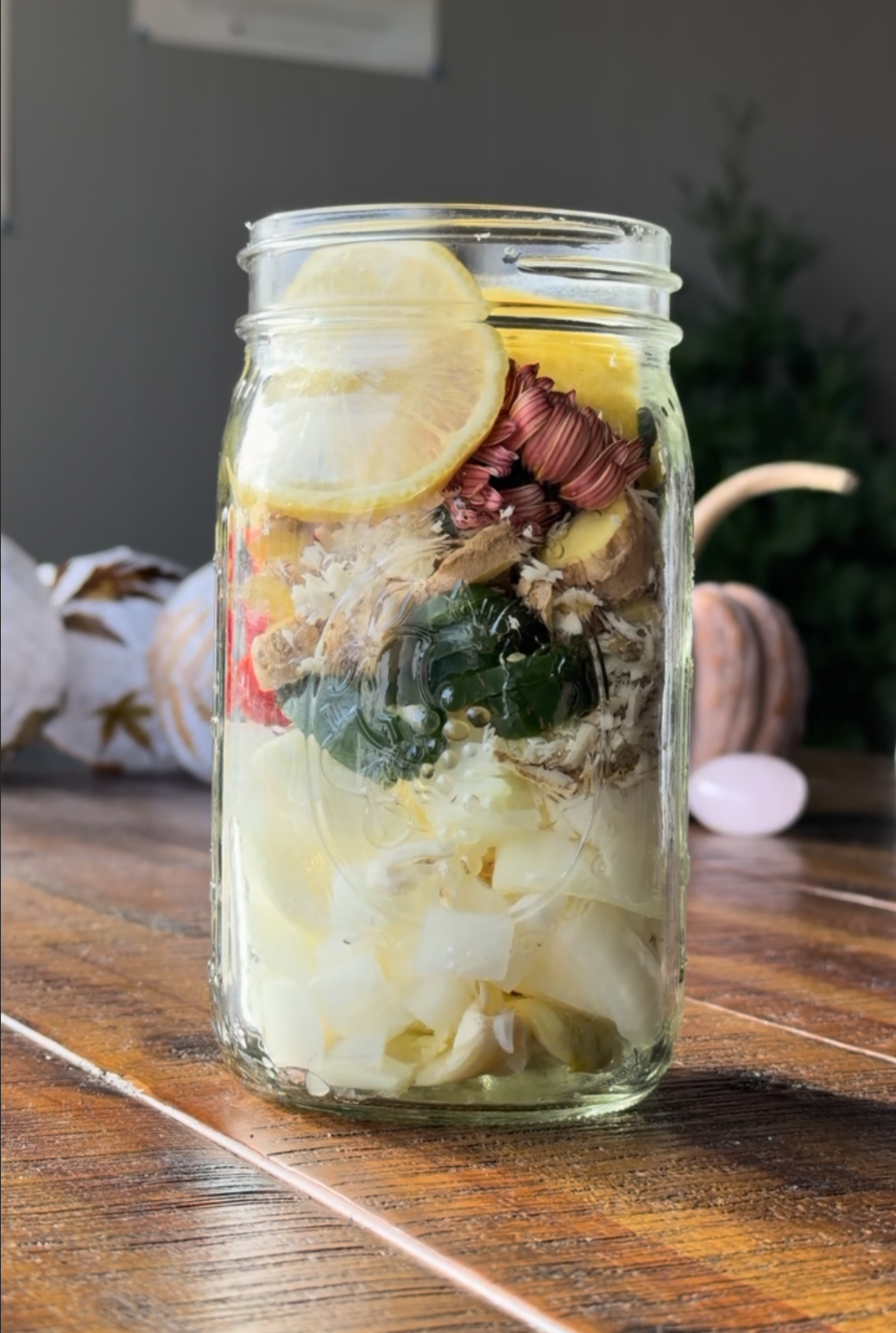 A mason jar of herbal fire cider ingredients on a wooden table